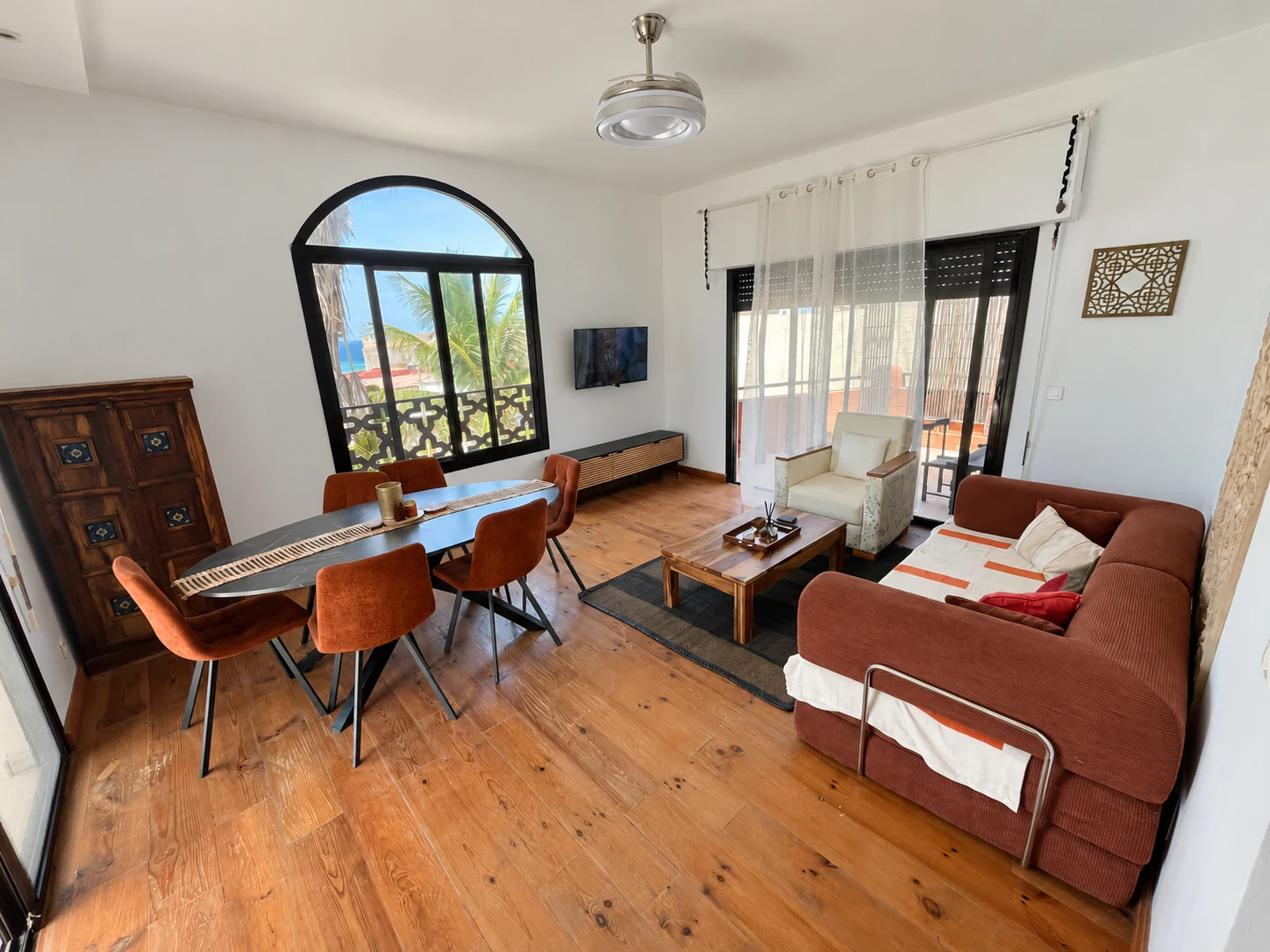 Ocean Suite — living and dining room with rust-coloured sofa and arched ocean-view window